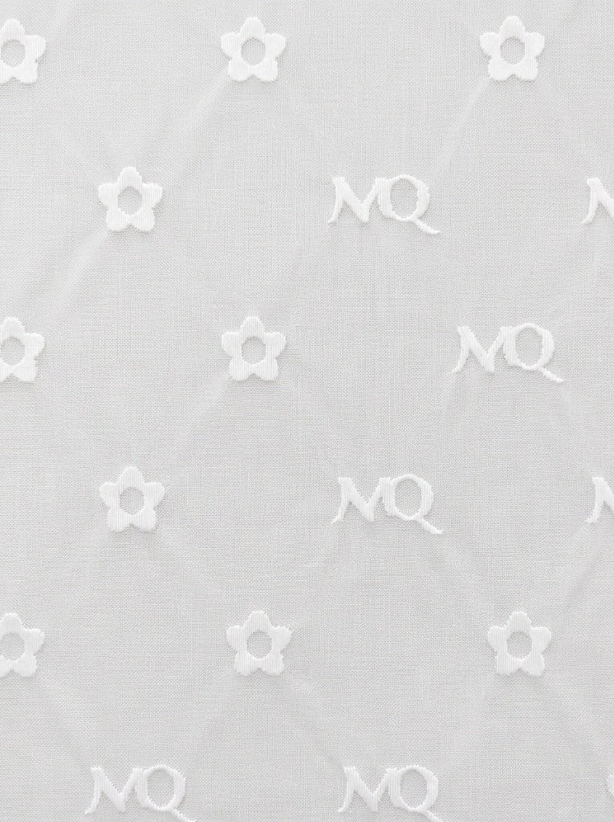 White textured fabric with a repeating pattern of small embroidered flowers and 'M.Q' monogram motifs.