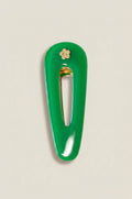 A glossy green hair clip with a small gold flower accent and gold-toned metal clasp, shown on a light beige background.