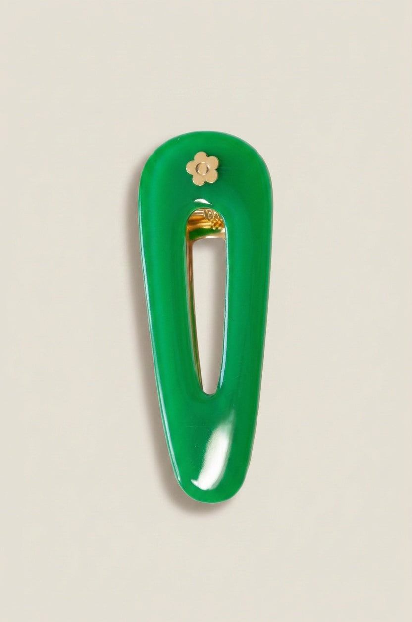 A glossy green hair clip with a small gold flower accent and gold-toned metal clasp, shown on a light beige background.